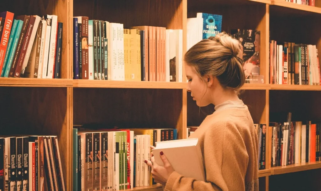 Seseorang sedang memilih buku dari rak di perpustakaan.